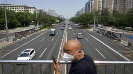 man wearing a face mask stands on a bridge over an expressway in Beijing
