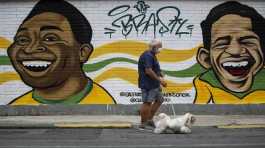 man walks his dog past a mural of Brazilian soccer stars Pele