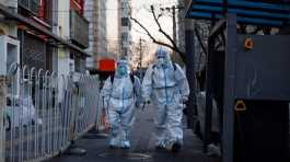 workers in protective suits walk in a street