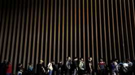People line up against a border wall