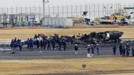 Police and Firefighters gather around the burn-out Japanese coast guard aircraft